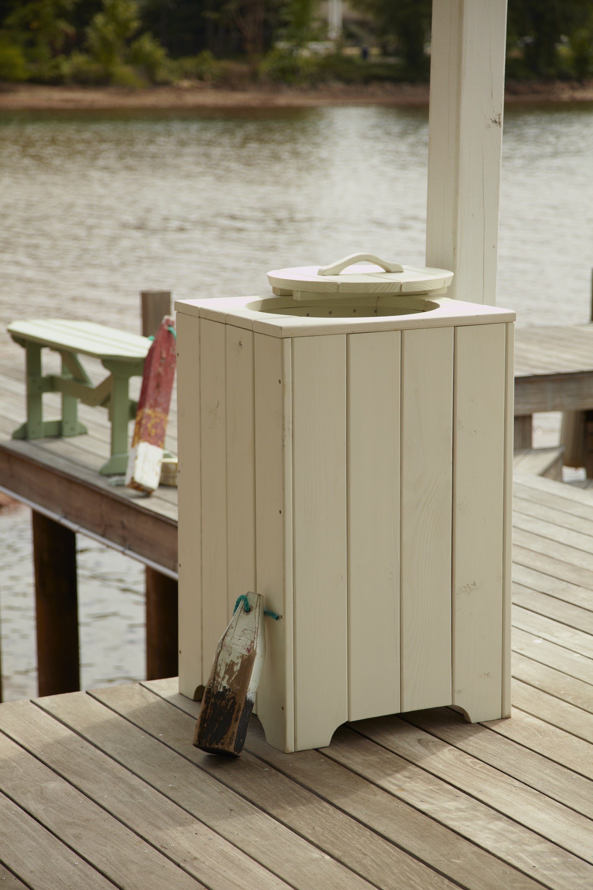 White outdoor patio trash bin with lid on a wooden dock beside the waterfront.