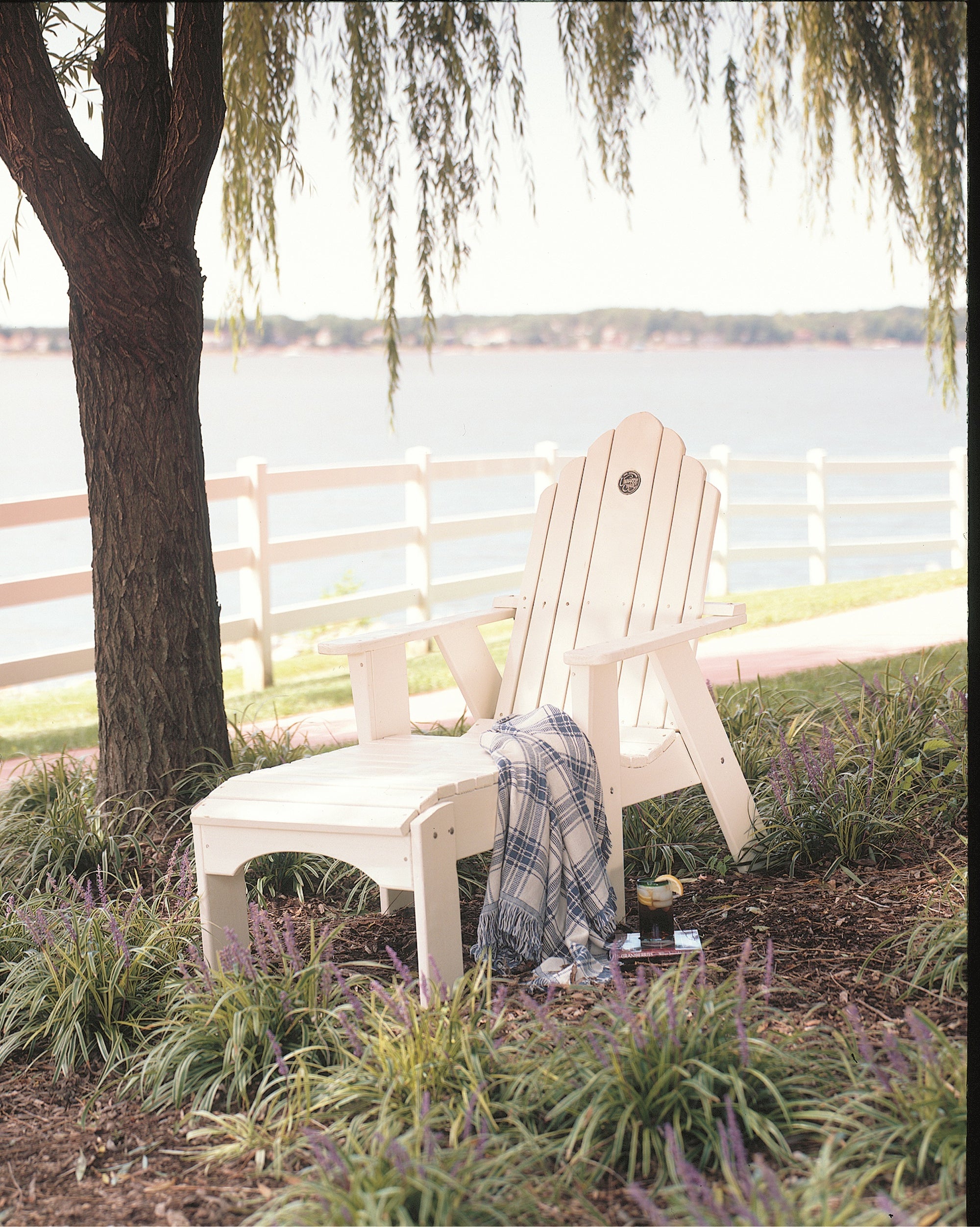 White Adirondack chair with matching ottoman and plaid throw blanket.